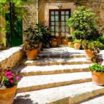 Mediterrane Steintreppe mit Terrakottatoepfen und Palettenkissen vor rustikalem Landhaus im Sueden