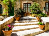 Mediterrane Steintreppe mit Terrakottatoepfen und Palettenkissen vor rustikalem Landhaus im Sueden