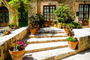 Mediterrane Steintreppe mit Terrakottatoepfen und Palettenkissen vor rustikalem Landhaus im Sueden