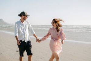 Paar spaziert lachend am Meer | Verlobungsringe